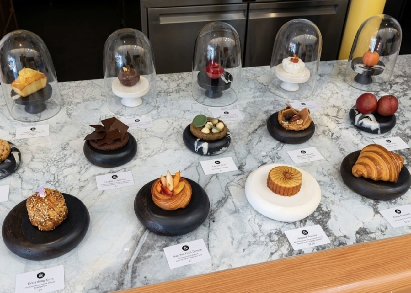 Assorted pastries and desserts displayed on black and white marble plates under glass domes on a marble countertop.