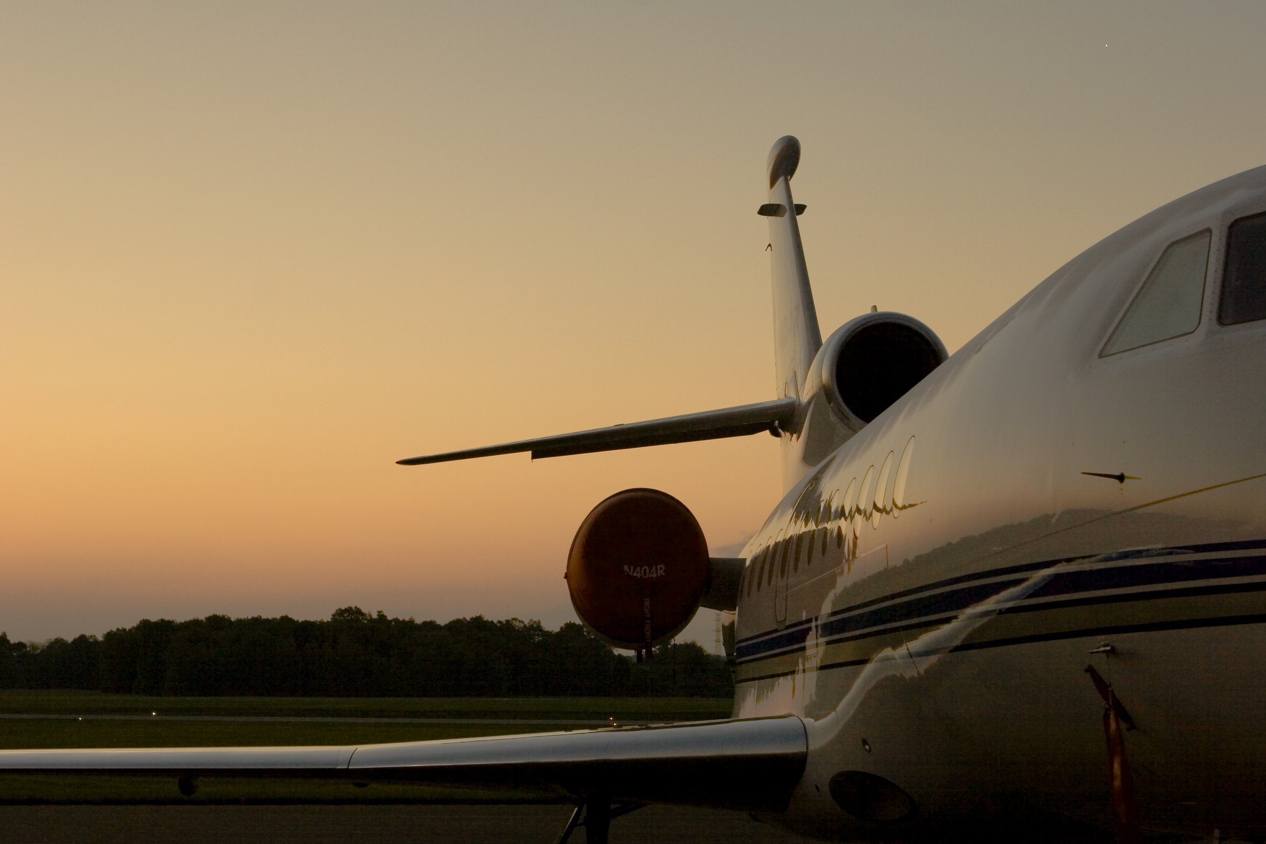 A private jet airplane on the runway during sunset with trees in the background.