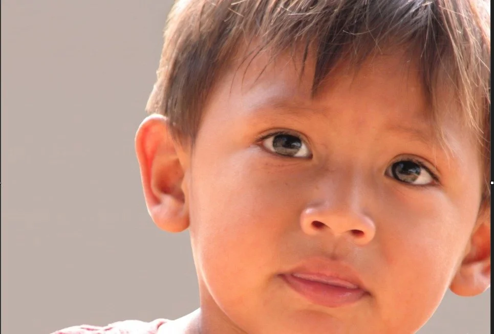 Close-up of a young child with light brown hair and blue eyes, looking slightly to the side with a neutral expression.