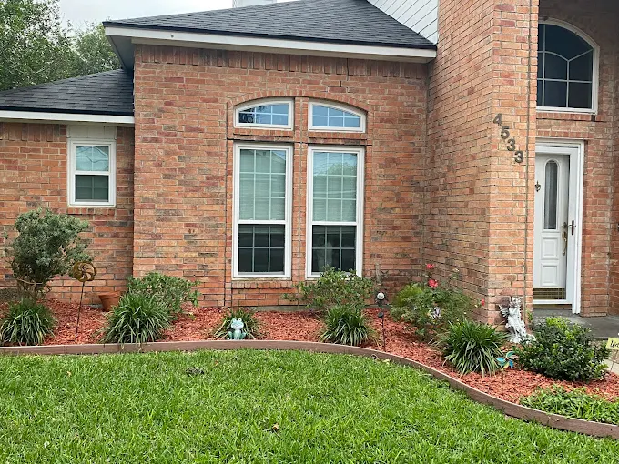 Front view of a brick house with a yard, including a large window, garden beds, and a white front door with house numbers 4533