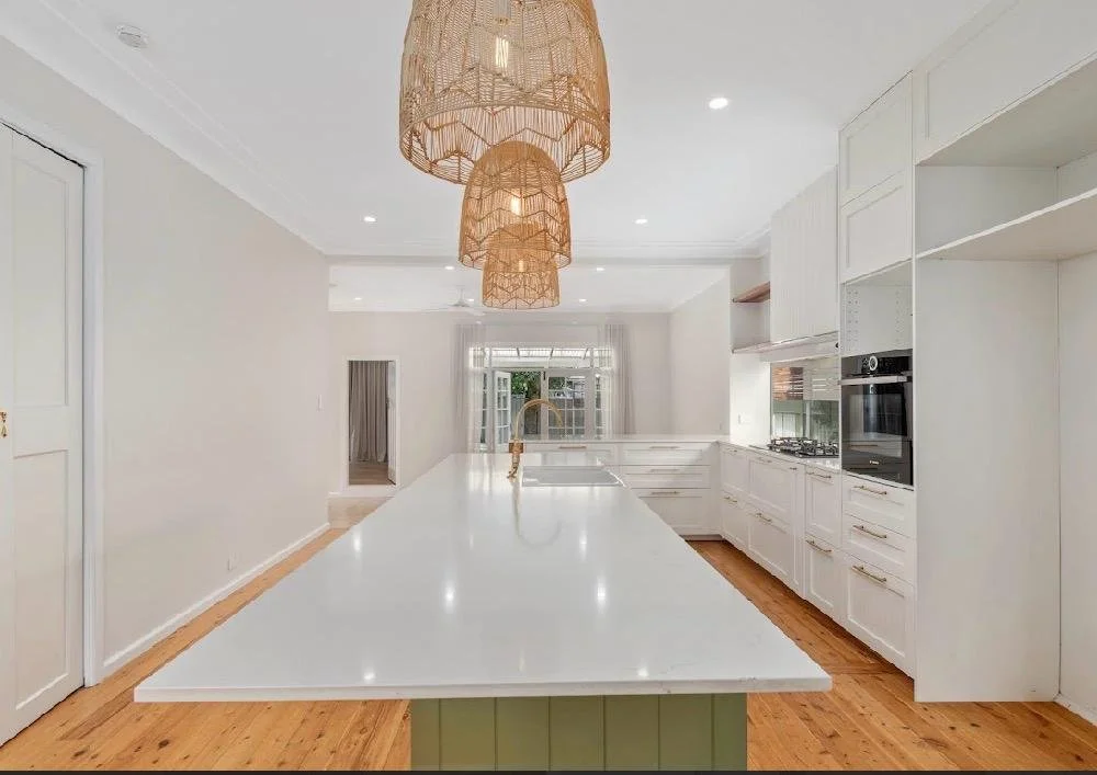 Bright kitchen with white countertops, white cabinets, built-in oven, and woven pendant light fixtures.