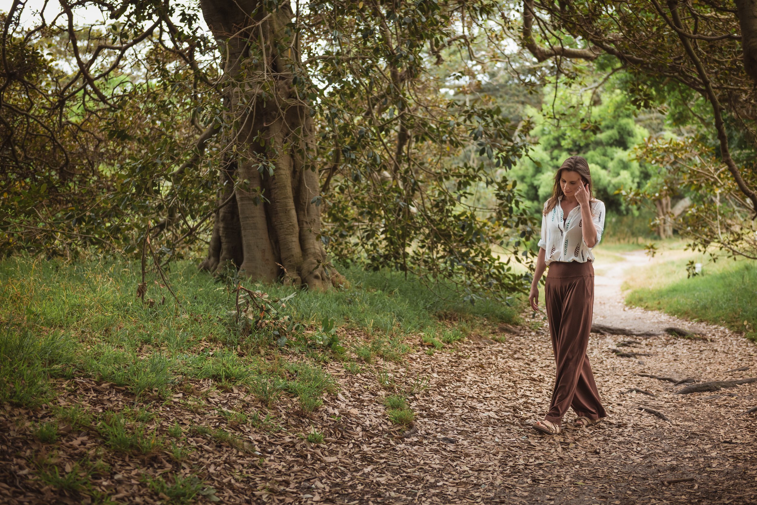 A woman walking on a dirt path surrounded by trees and greenery in a park or forest.