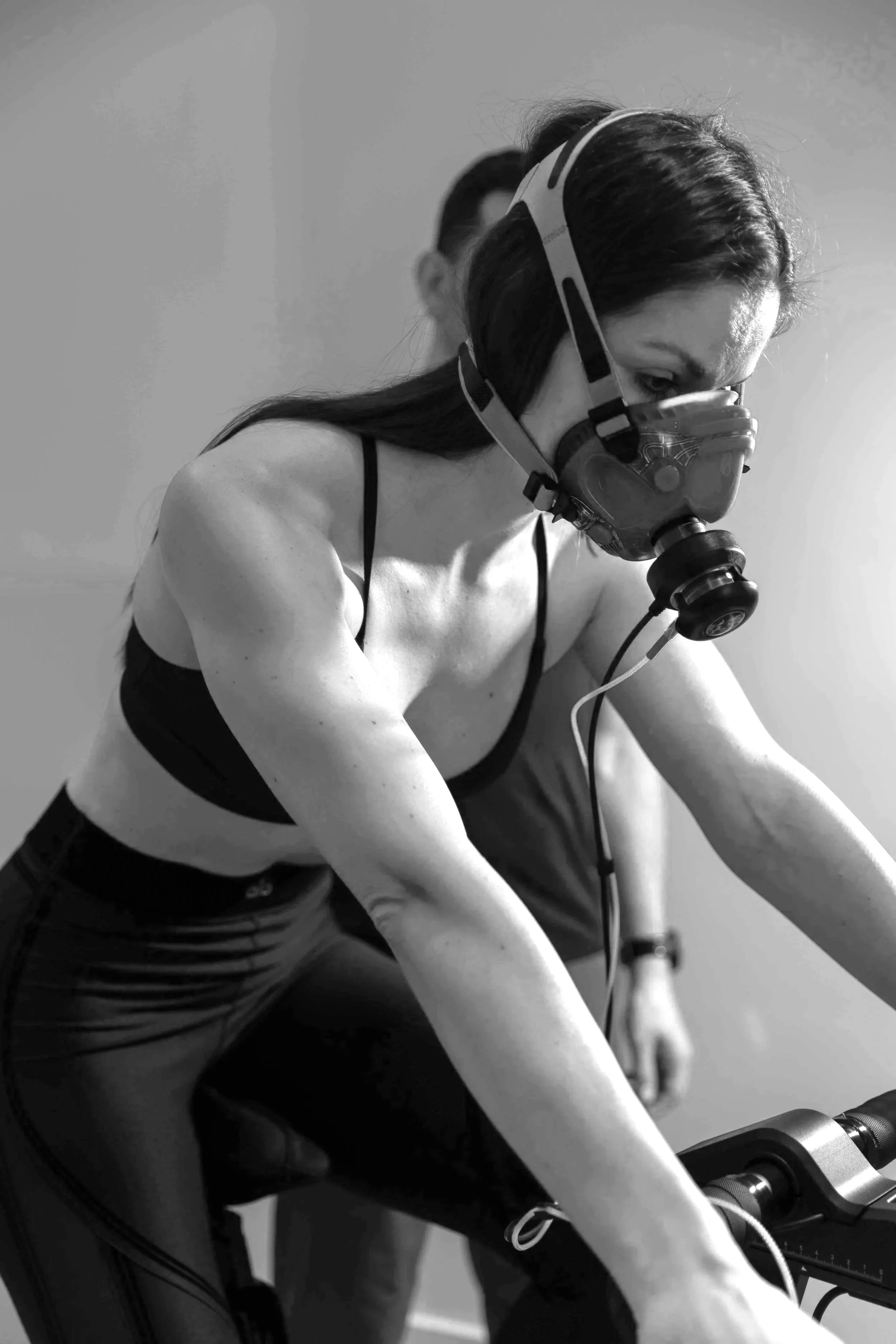 A woman wearing a sports bra and leggings, with a mask and helmet, riding a stationary bike.