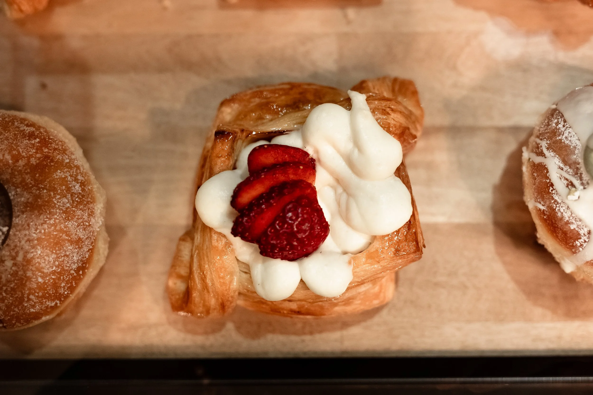 A pastry topped with strawberries, whipped cream, and small dollops of whipped cream on a wooden surface.