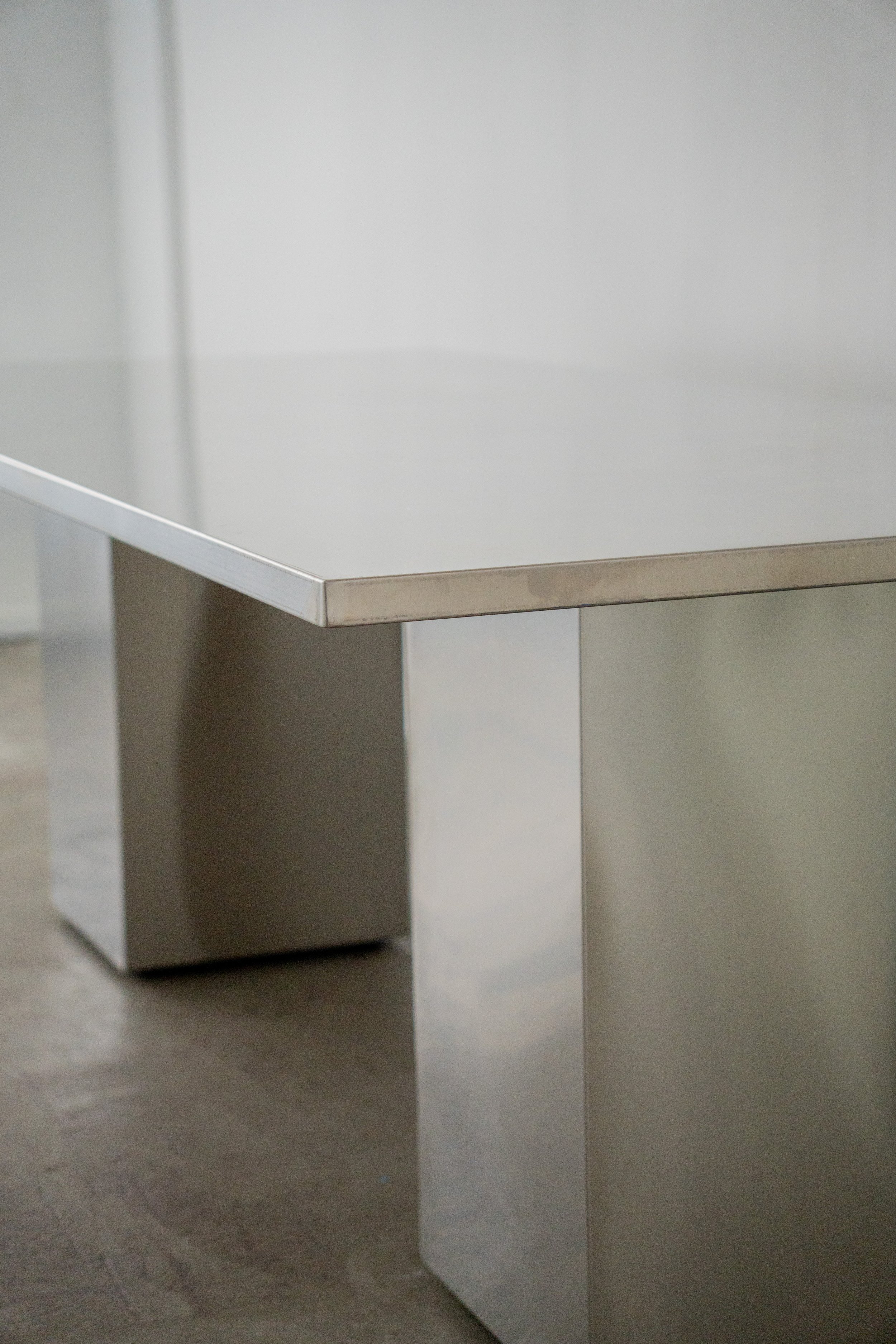 Close-up of a modern stainless steel table with a flat top and rectangular legs, situated in a minimalistic room.