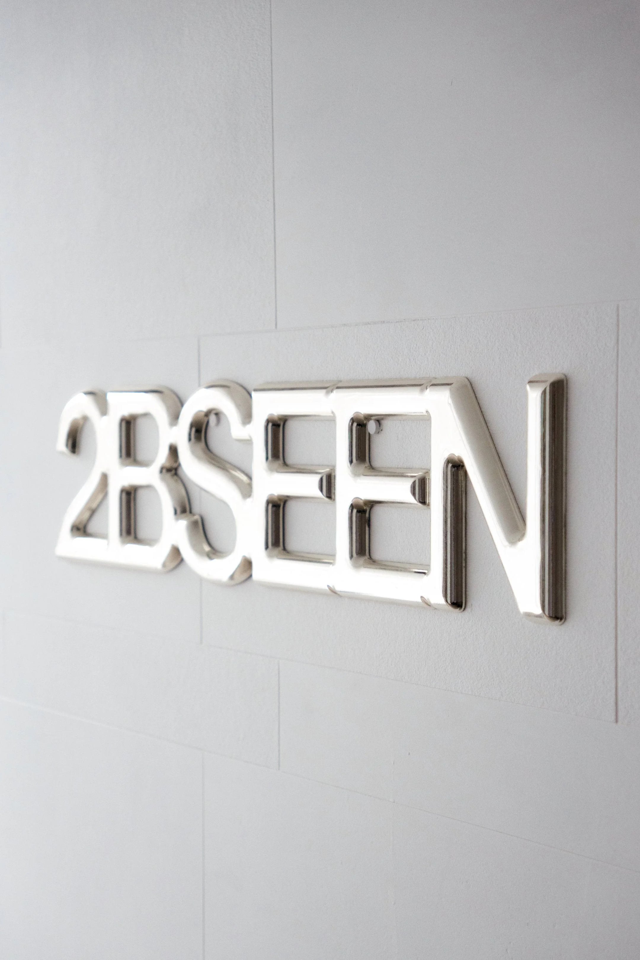 Close-up of a neon sign displaying the word '2BSEE' mounted on a light-colored wall.