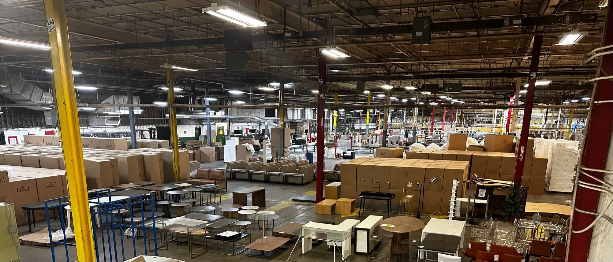 Warehouse store with furniture displays, boxes, tables, chairs, and lighting fixtures.