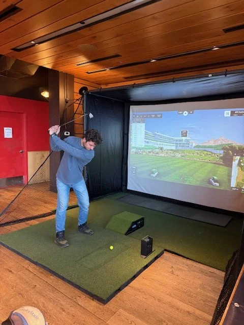 Person swinging a golf club on an indoor golf simulator.