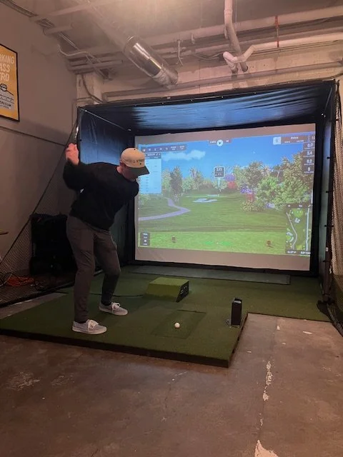 Person swinging a golf club on an indoor golf simulator.