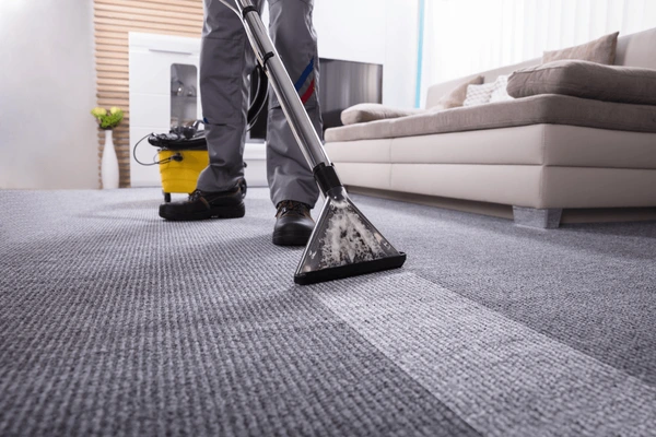 Person professionally cleaning a gray carpet with a vacuum cleaner in a living room.