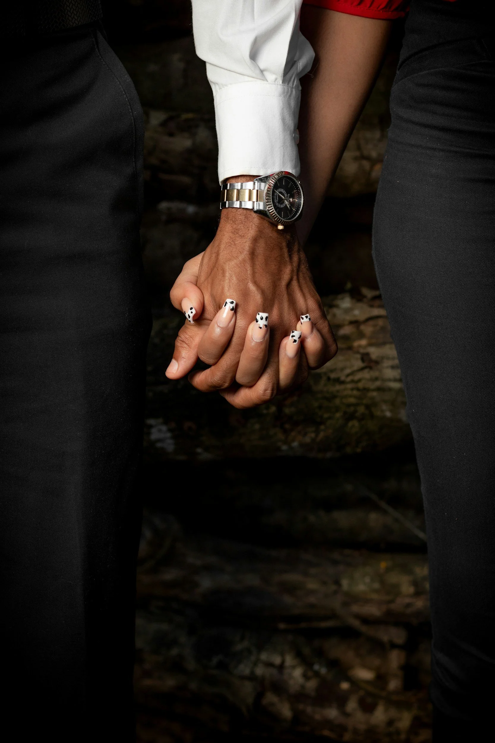 Close-up of two people holding hands against a dark, rocky background.
