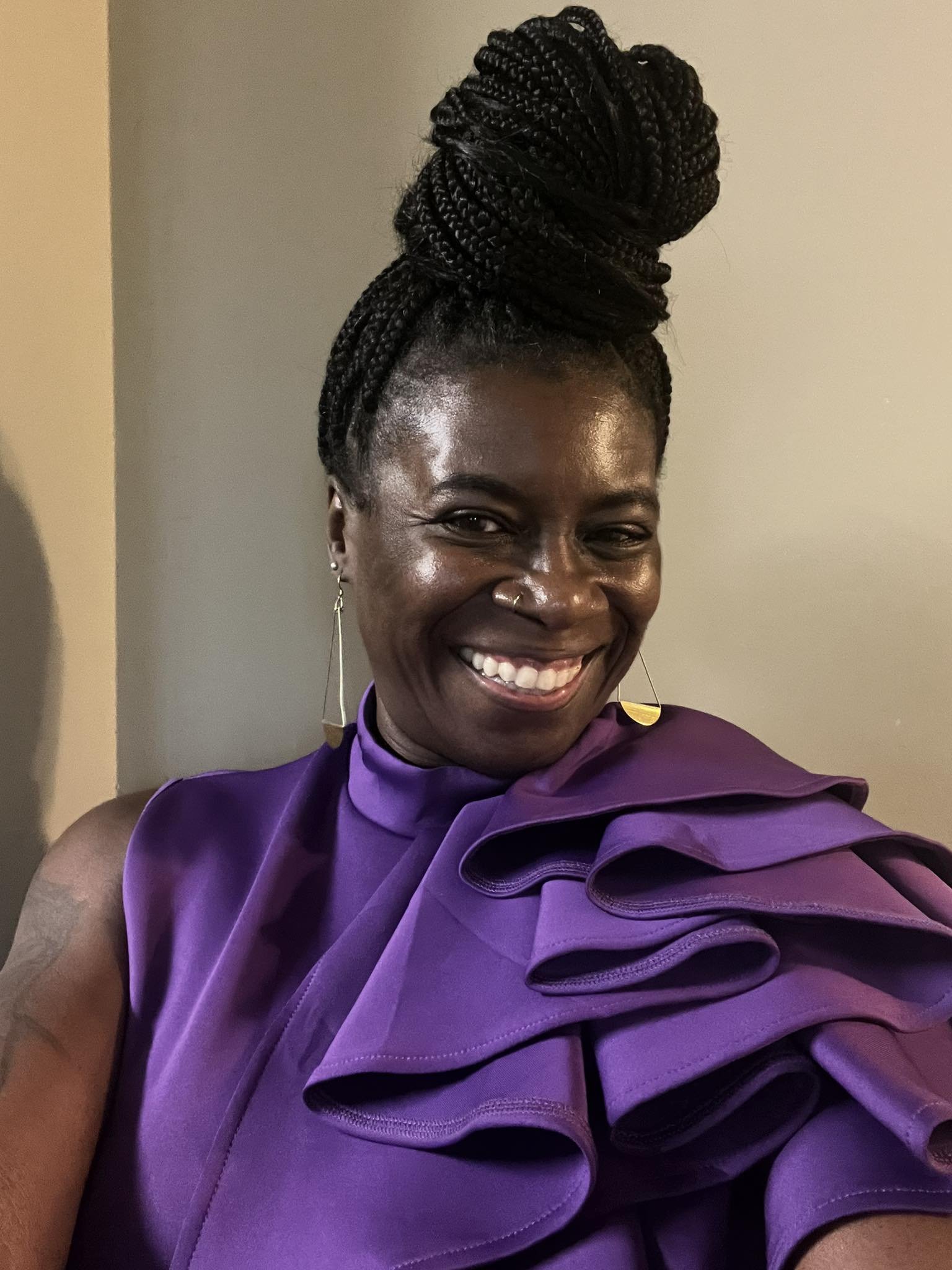 Karyn J. Johnson smiling, wearing a purple dress with her hair styled in a high braided bun.