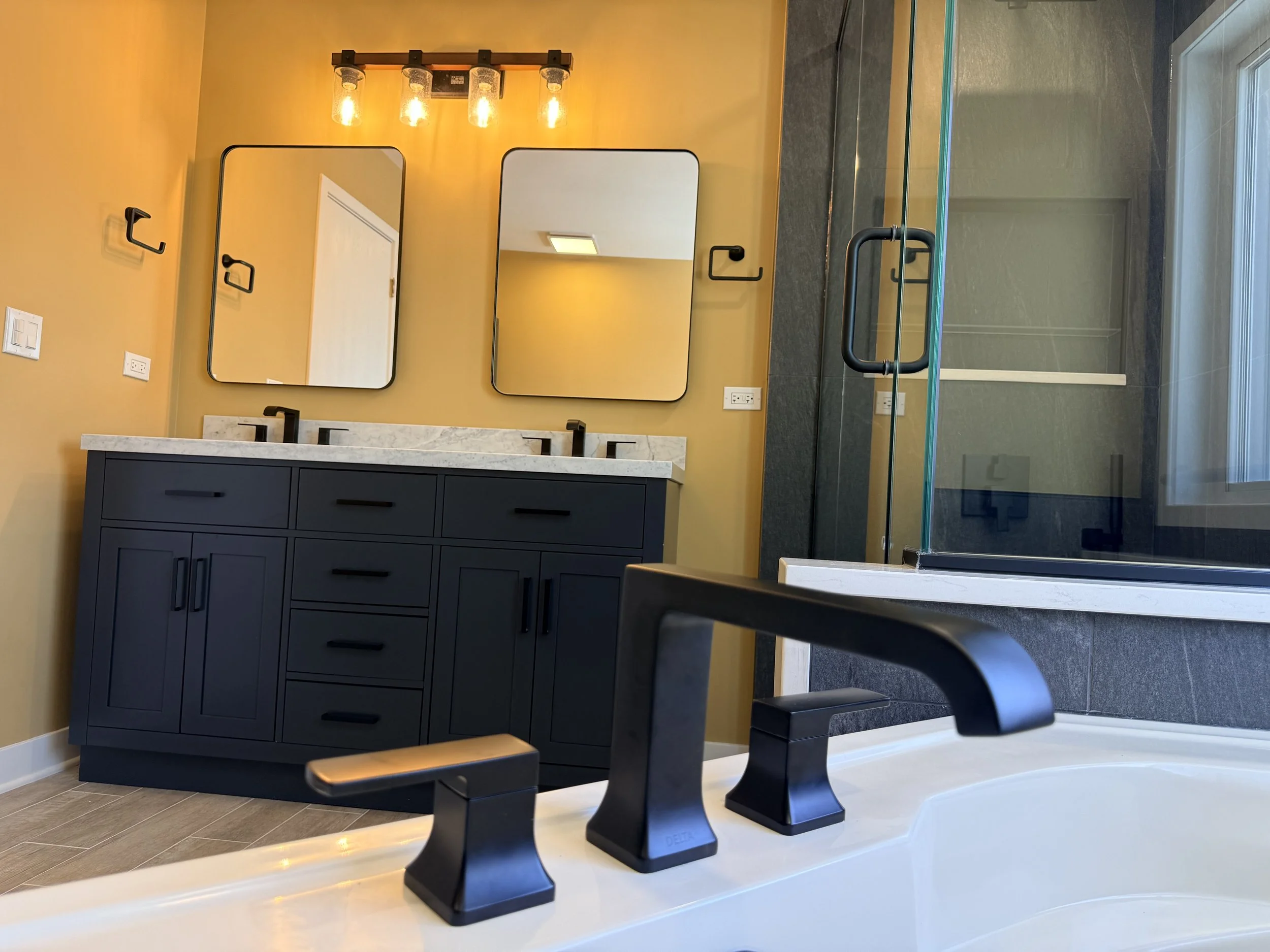 Luxury bathroom renovation with double sink vanity, matte black fixtures, quartz countertop, modern mirrors, and walk-in glass shower.