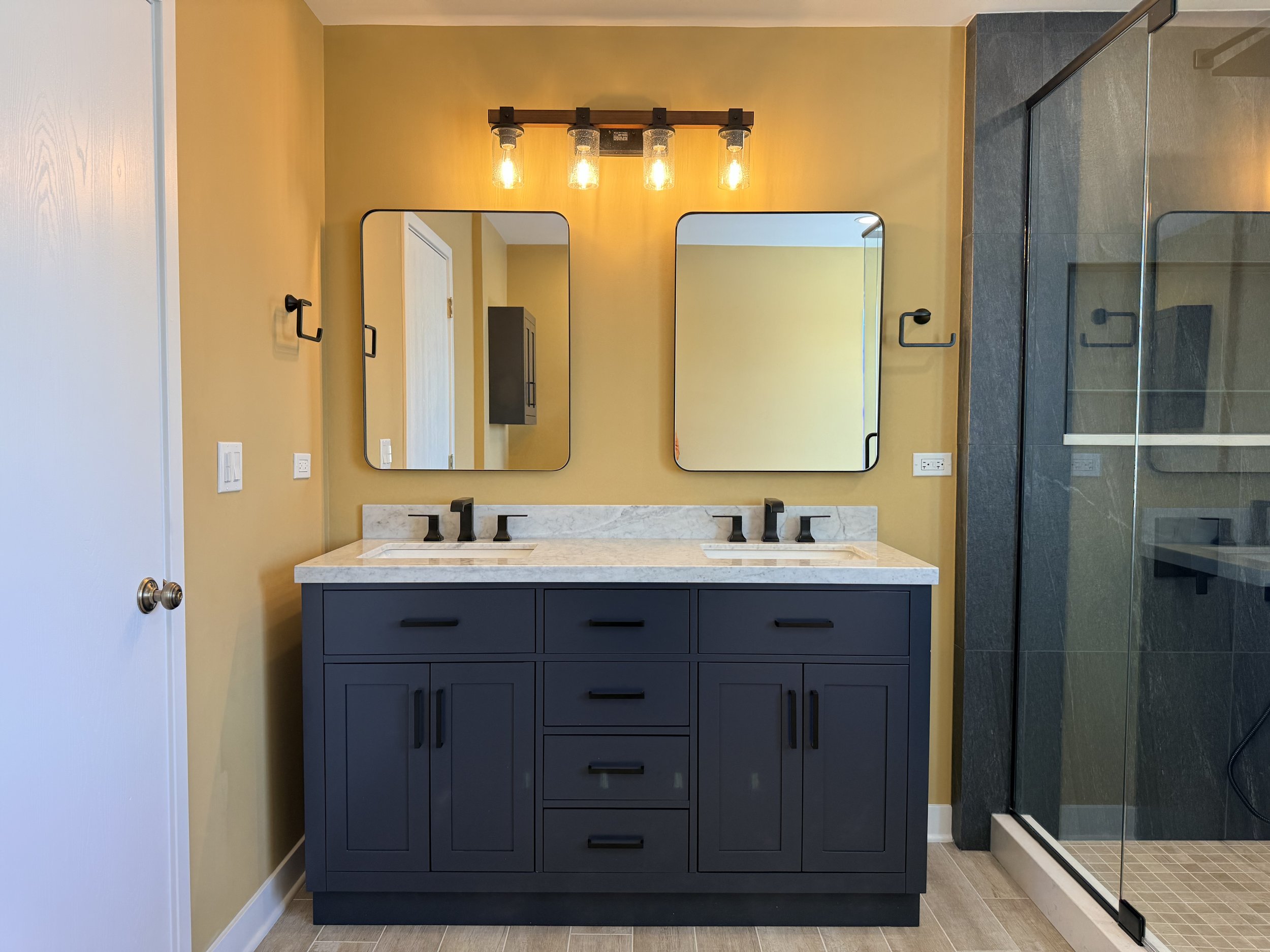 Luxury bathroom renovation with double sink vanity, quartz countertop, matte black fixtures, rectangular mirrors, and glass-enclosed walk-in shower.
