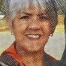 A smiling woman with short, gray hair wearing earrings and an orange necklace.