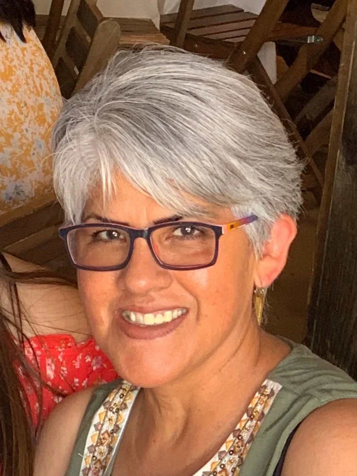 A smiling woman with short, gray hair wearing earrings and an orange necklace.