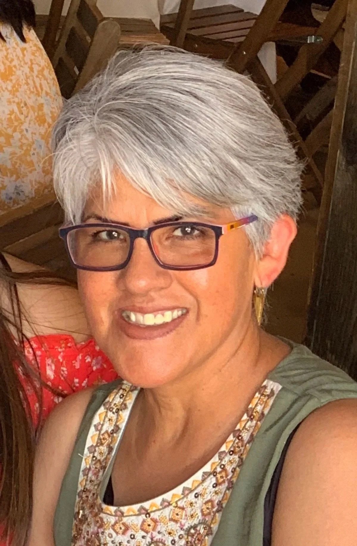 A smiling woman with short, gray hair wearing earrings and an orange necklace.