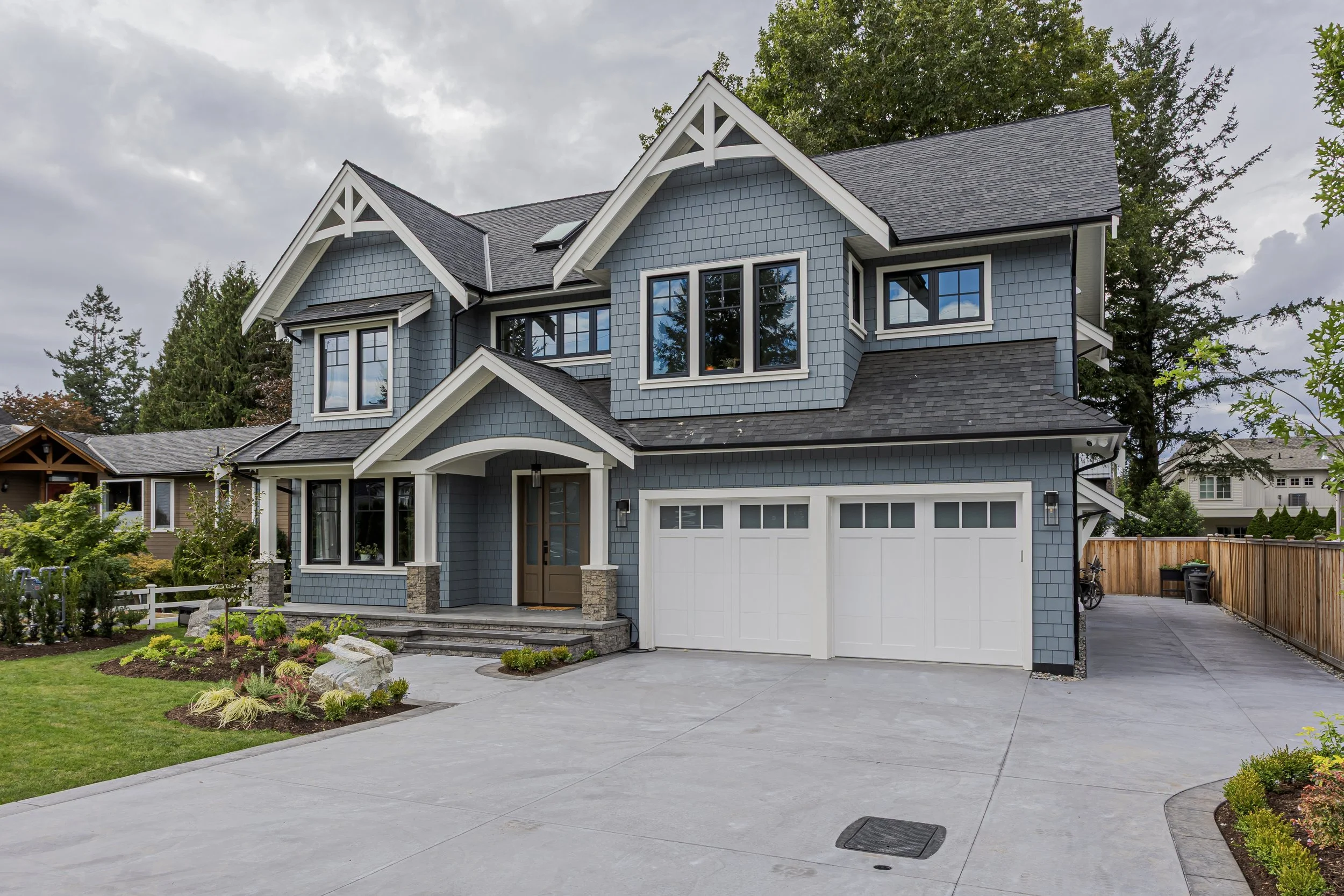 Two-storey craftsman-style home in Fort Langley with blue shingle siding, a covered entry, and a double garage overlooking a landscaped driveway.