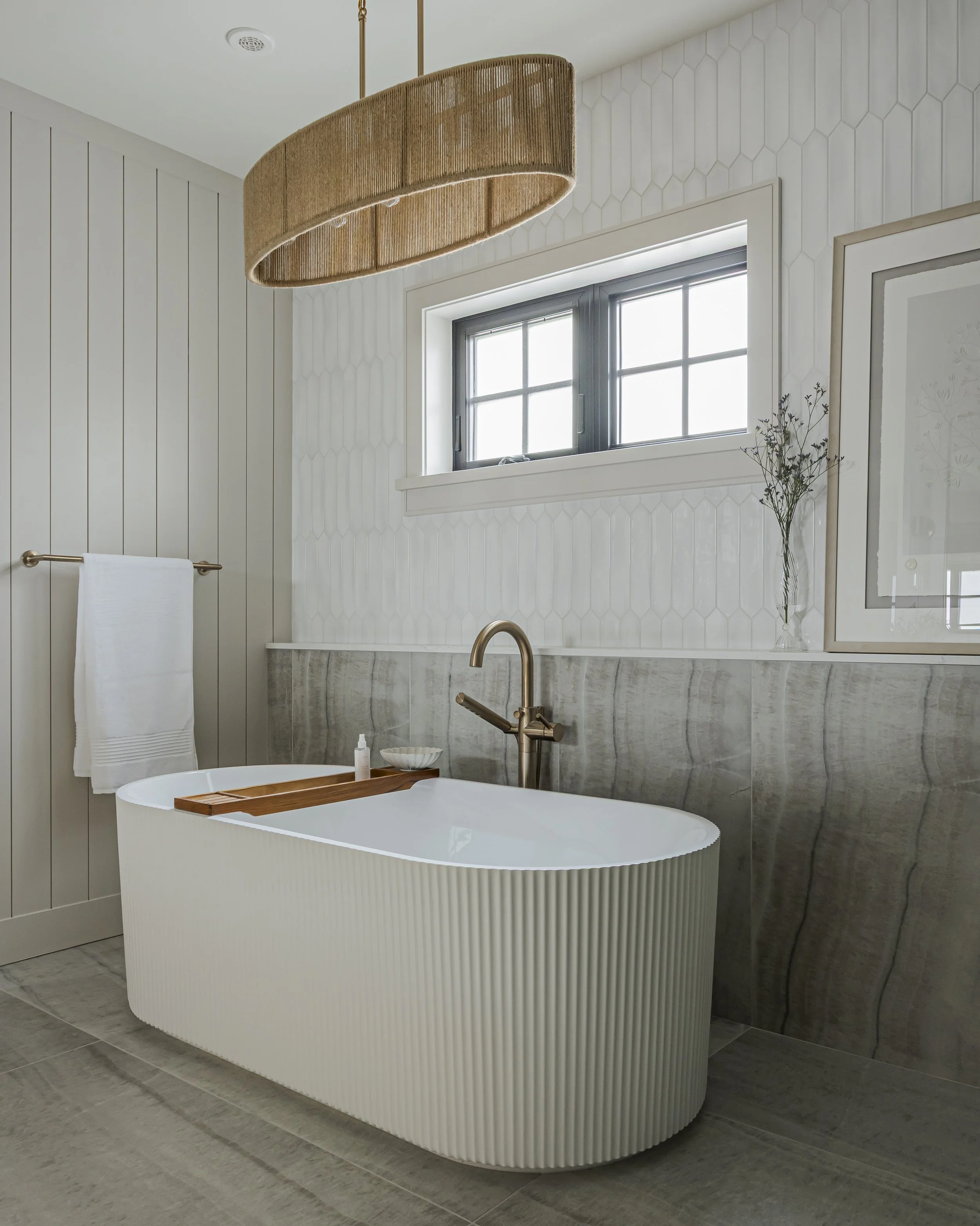 Bathroom with a freestanding ribbed soaking tub, brass floor-mounted faucet, and a patterned tile accent wall