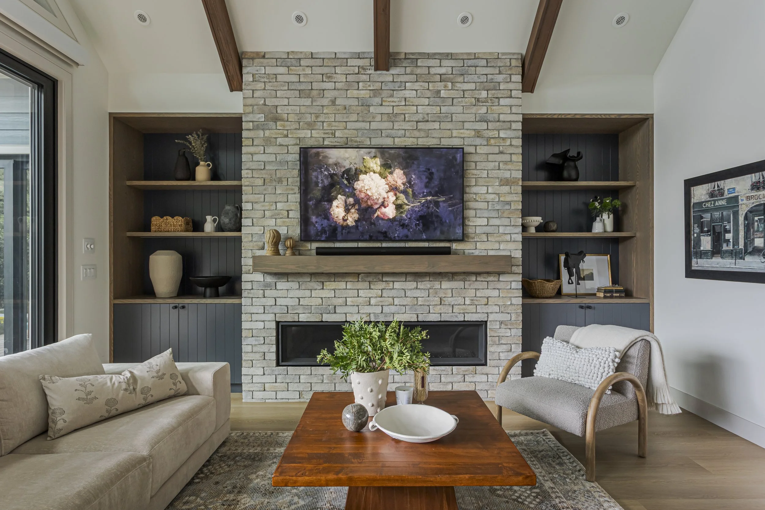 Living room with a stone fireplace, wall-mounted TV, built-in navy cabinetry and shelving, and a neutral sectional sofa