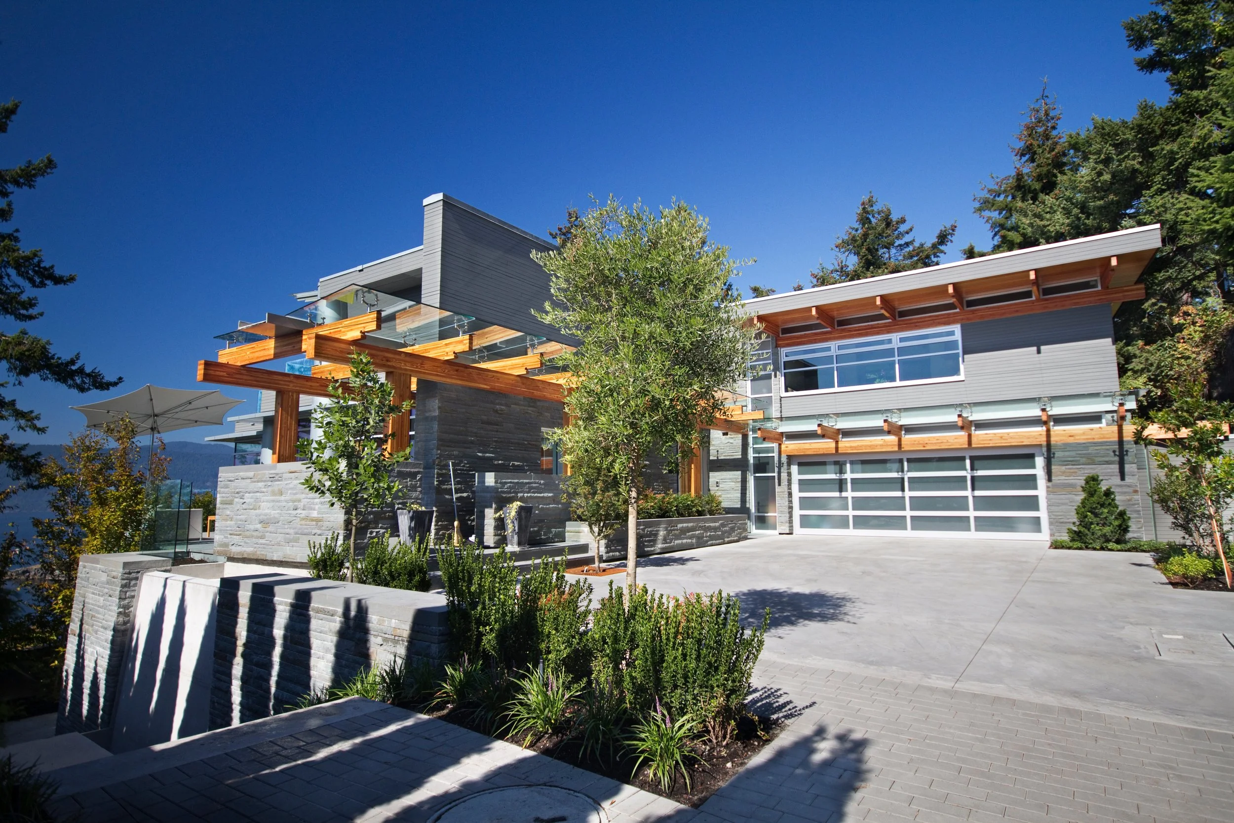 Modern two-storey home in Horseshoe Bay, West Vancouver, with a cedar pergola, glass railings, and stone entry accents