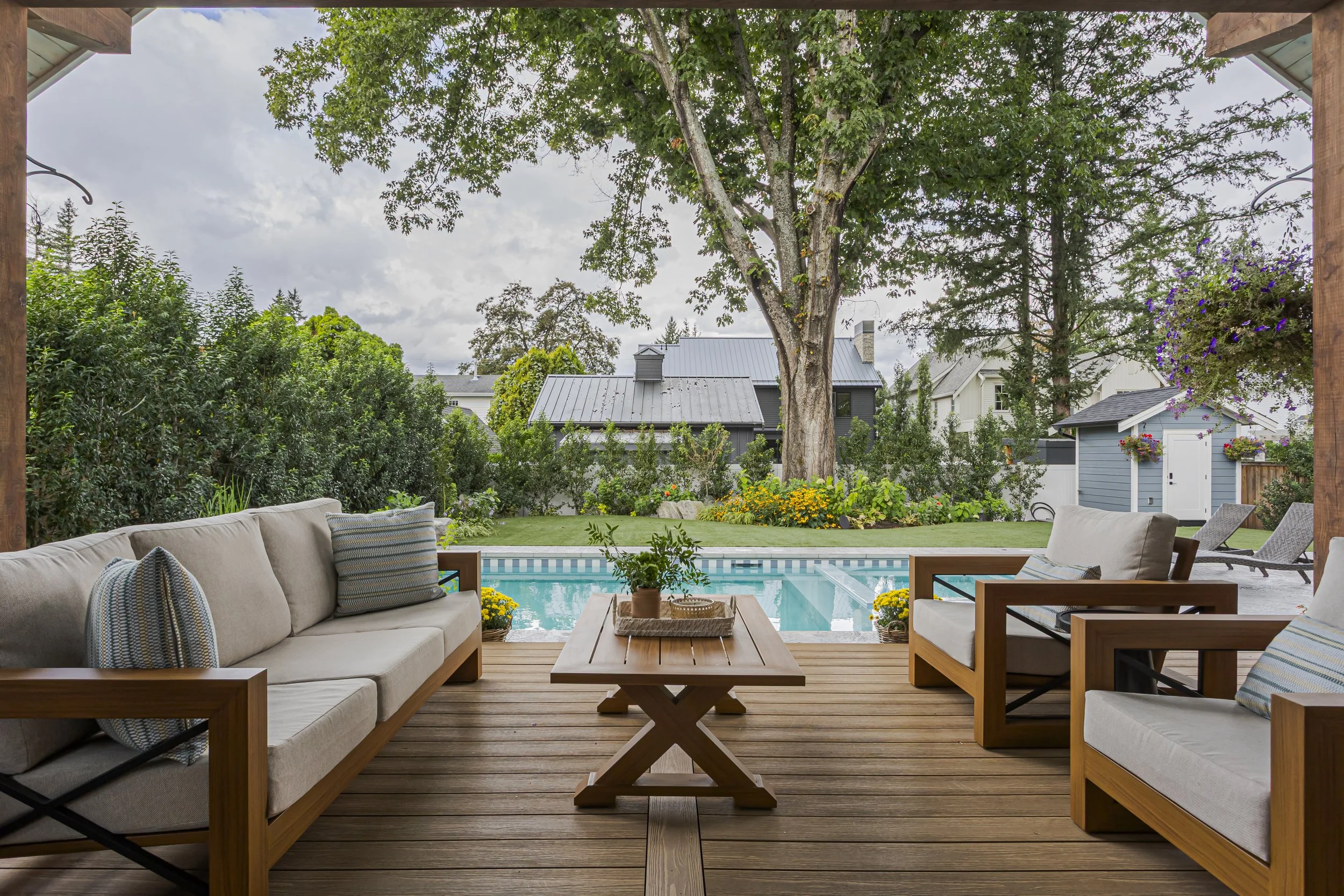 Covered outdoor patio with a wood-framed sectional and lounge chairs overlooking the pool and backyard garden
