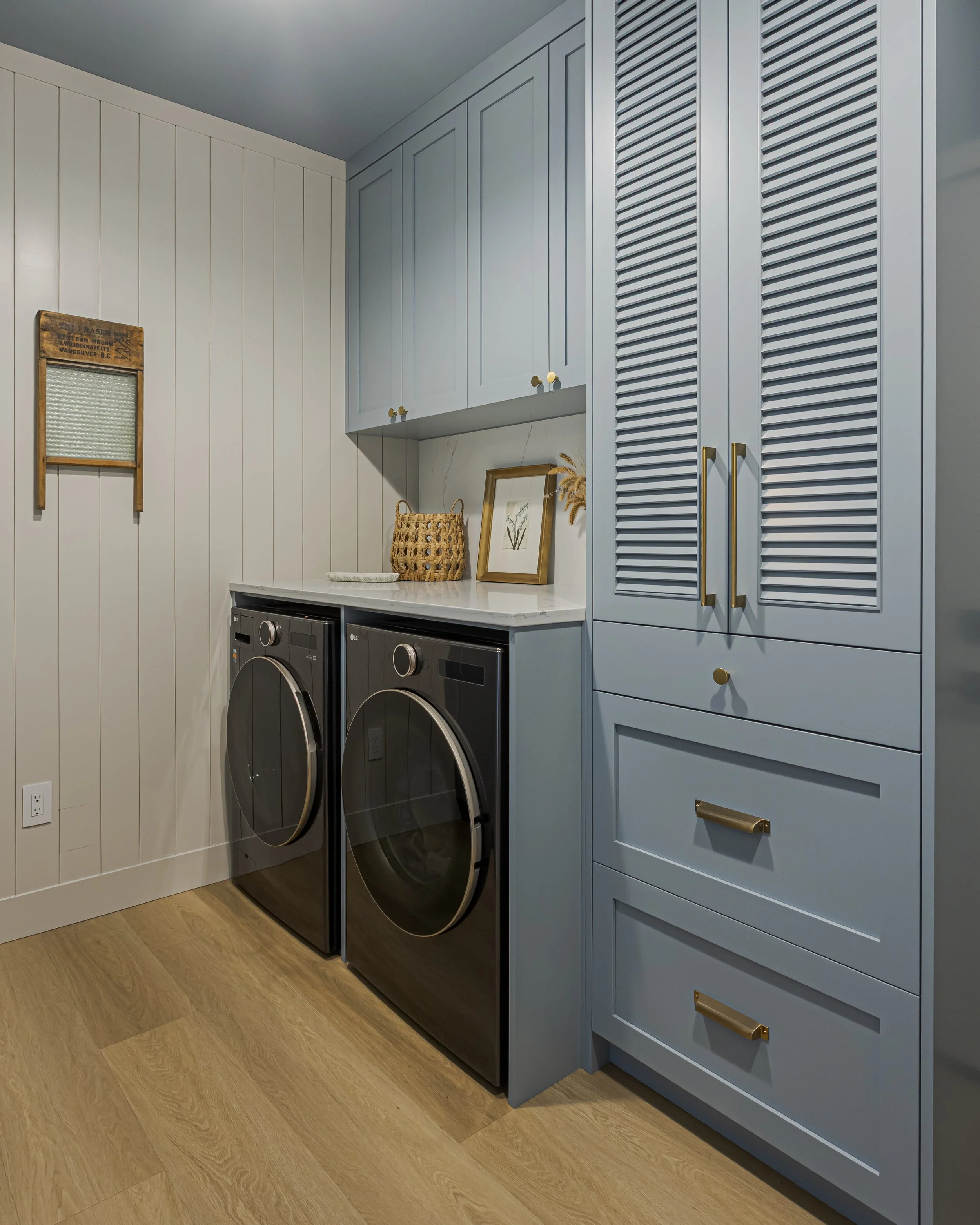 Laundry room with light blue cabinetry, louvered storage doors, and a stacked washer and dryer