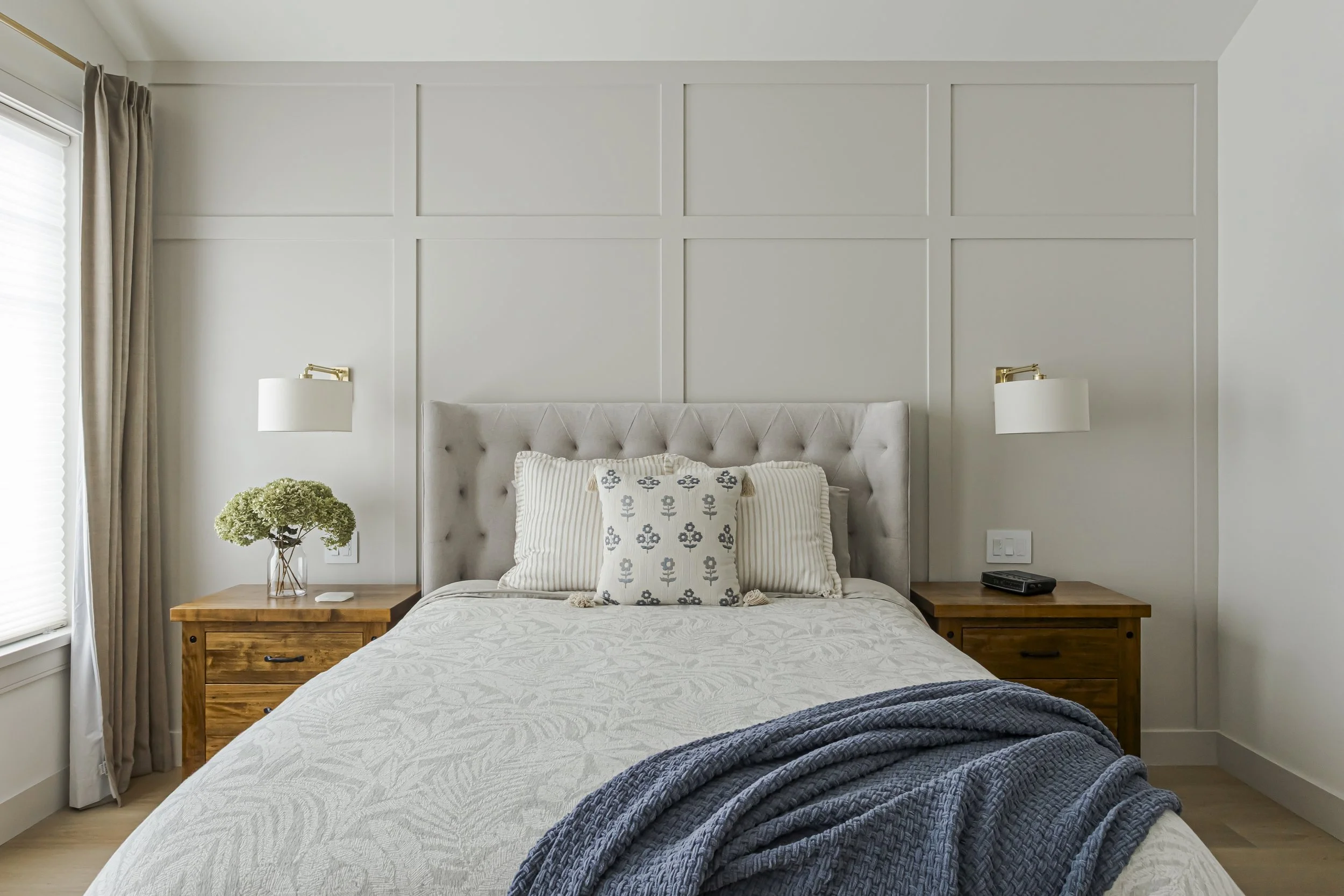 Bedroom with an upholstered tufted headboard, wood nightstands, and brass wall sconces.