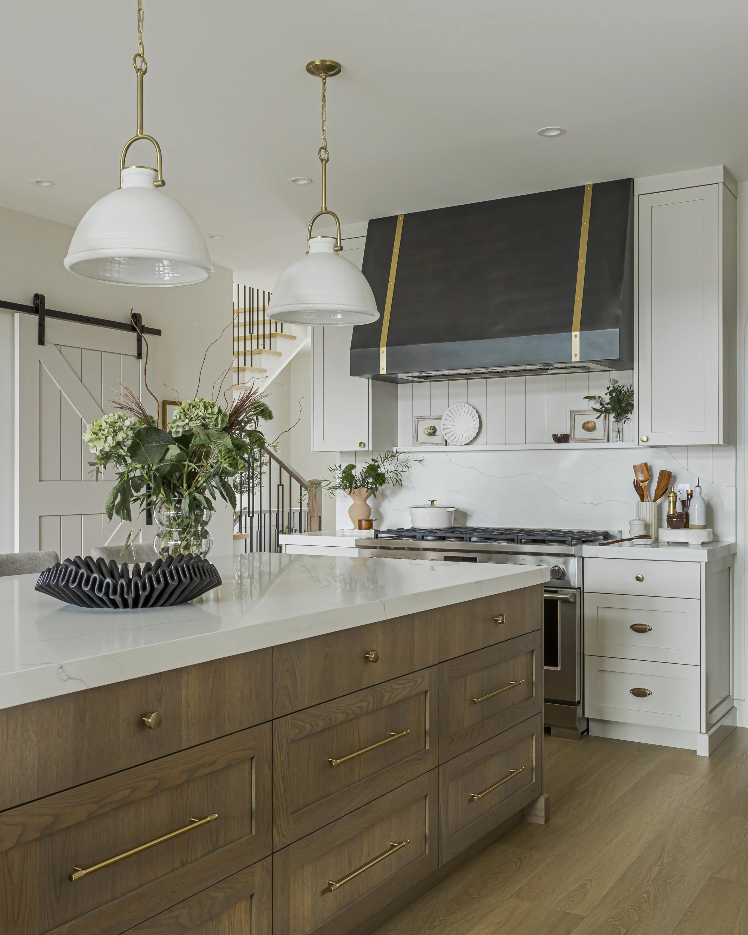 Kitchen with a dark wood island, brass hardware, a charcoal range hood with brass trim, and white perimeter cabinetry