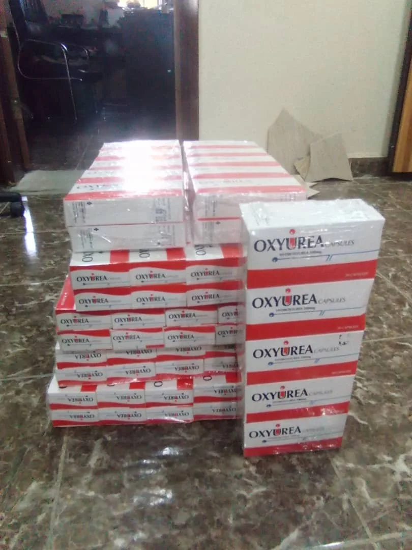 Stacked boxes labeled 'OXYUREA' on a marble floor inside a room, with an open doorway in the background.