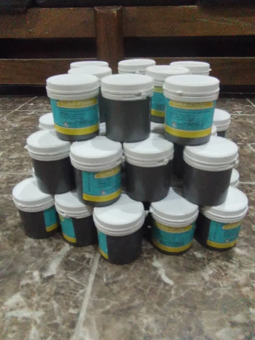 A pyramid of black jars with white lids and blue labels on a tiled floor.