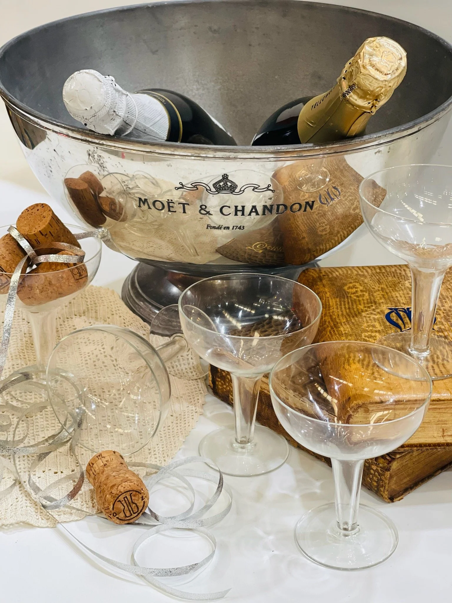 A silver bucket labeled Moët & Chandon with multiple bottles of champagne inside, surrounded by empty champagne glasses, corks, and decorative ribbons on a table.