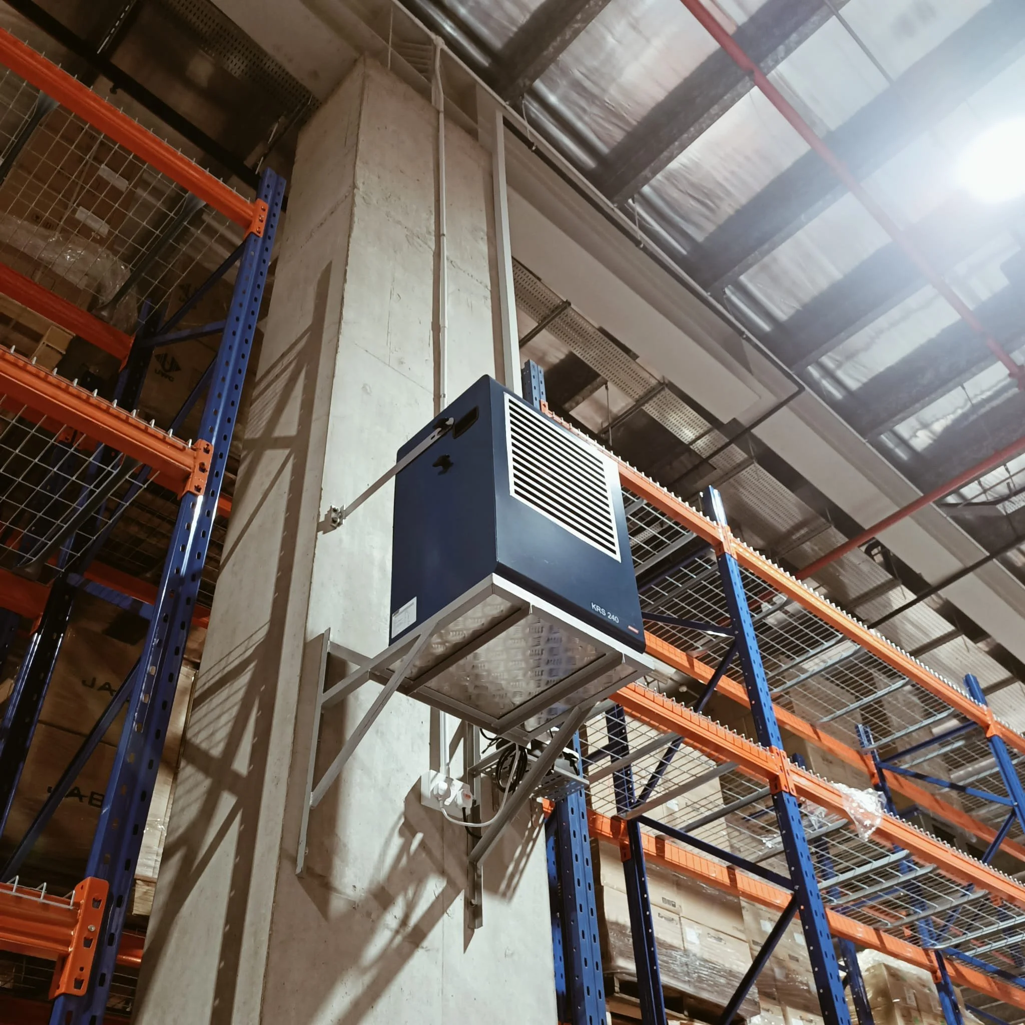 An industrial warehouse with orange and blue shelving units and a blue dehumidifier unit mounted on the wall.