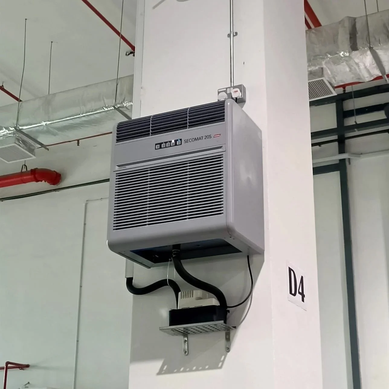 An industrial dehumidifier unit mounted on a white wall in a commercial building, with visible ductwork and piping.