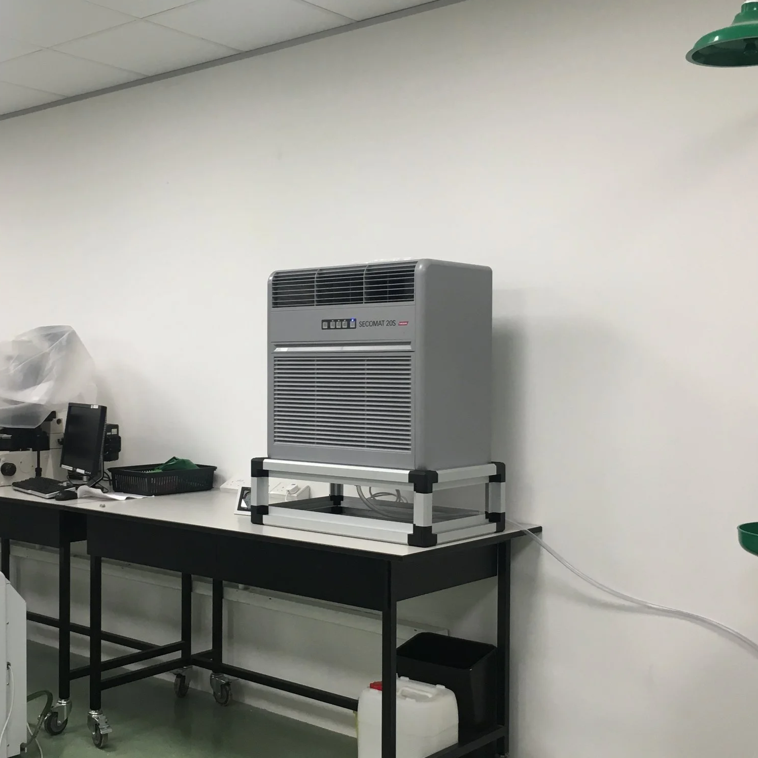 A laboratory setting with a large dehumidifier on a black and white work table, with various laboratory equipment and supplies around.