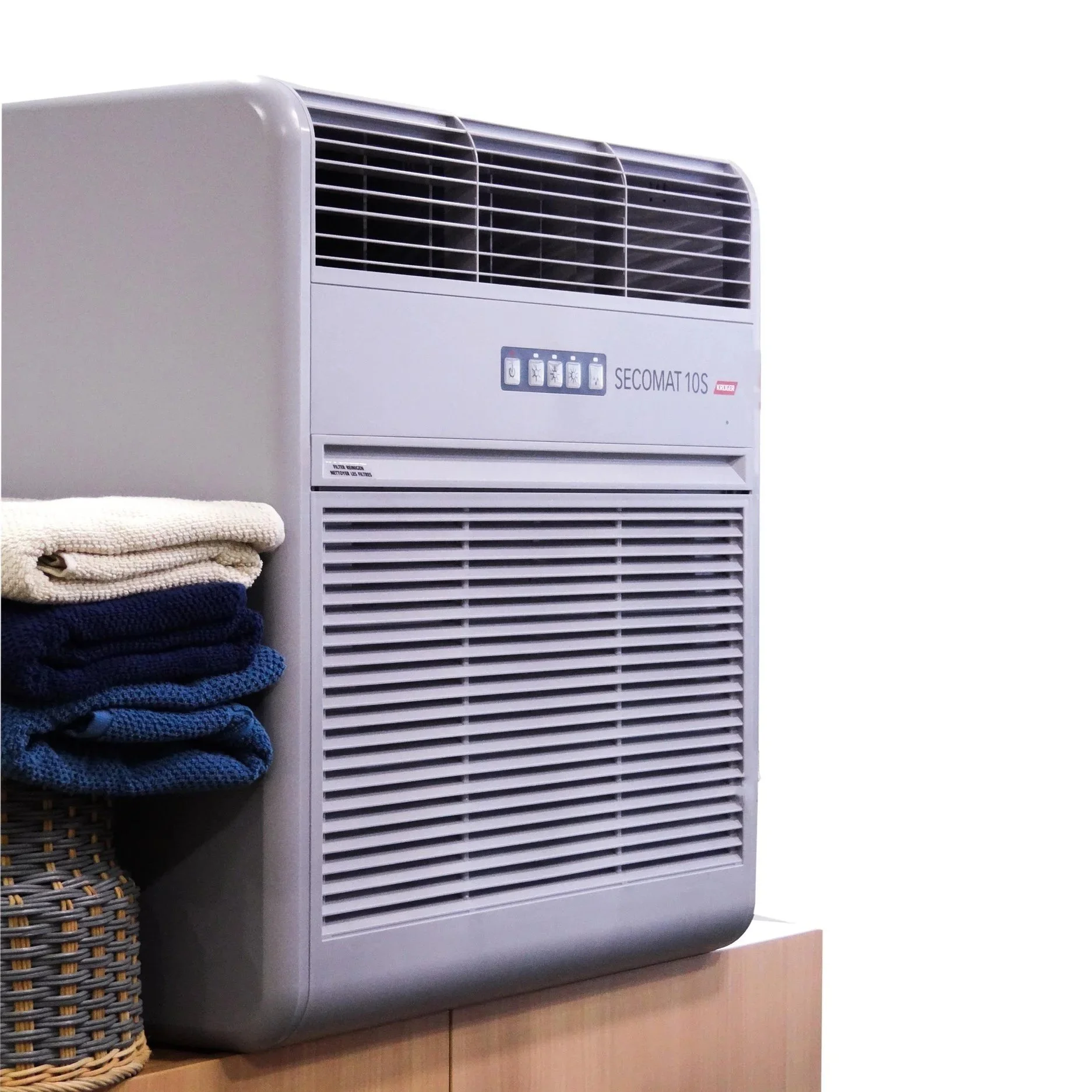 A wall-mounted dehumidifier unit labeled 'SECOMAT 10S' beside a woven basket with folded towels. The unit is grey with vents and control buttons.