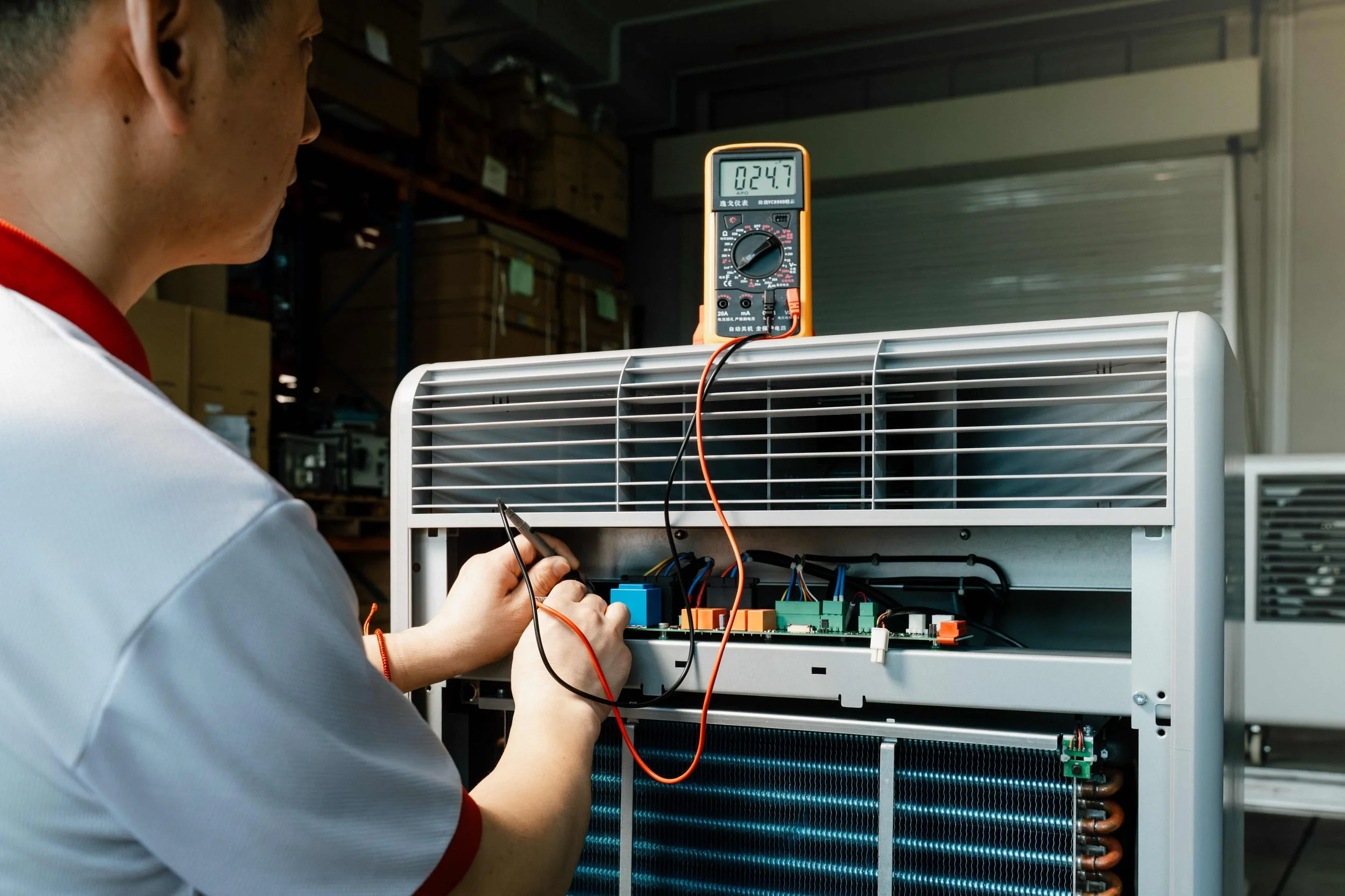 Technician working on a dehumidifier unit, measuring electrical current with a multimeter.