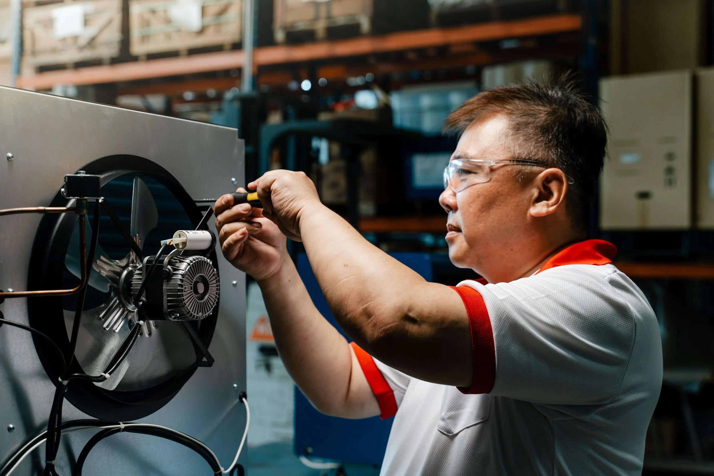 A technician wearing safety glasses works on a dehumidifier unit in a workshop, using a screwdriver.