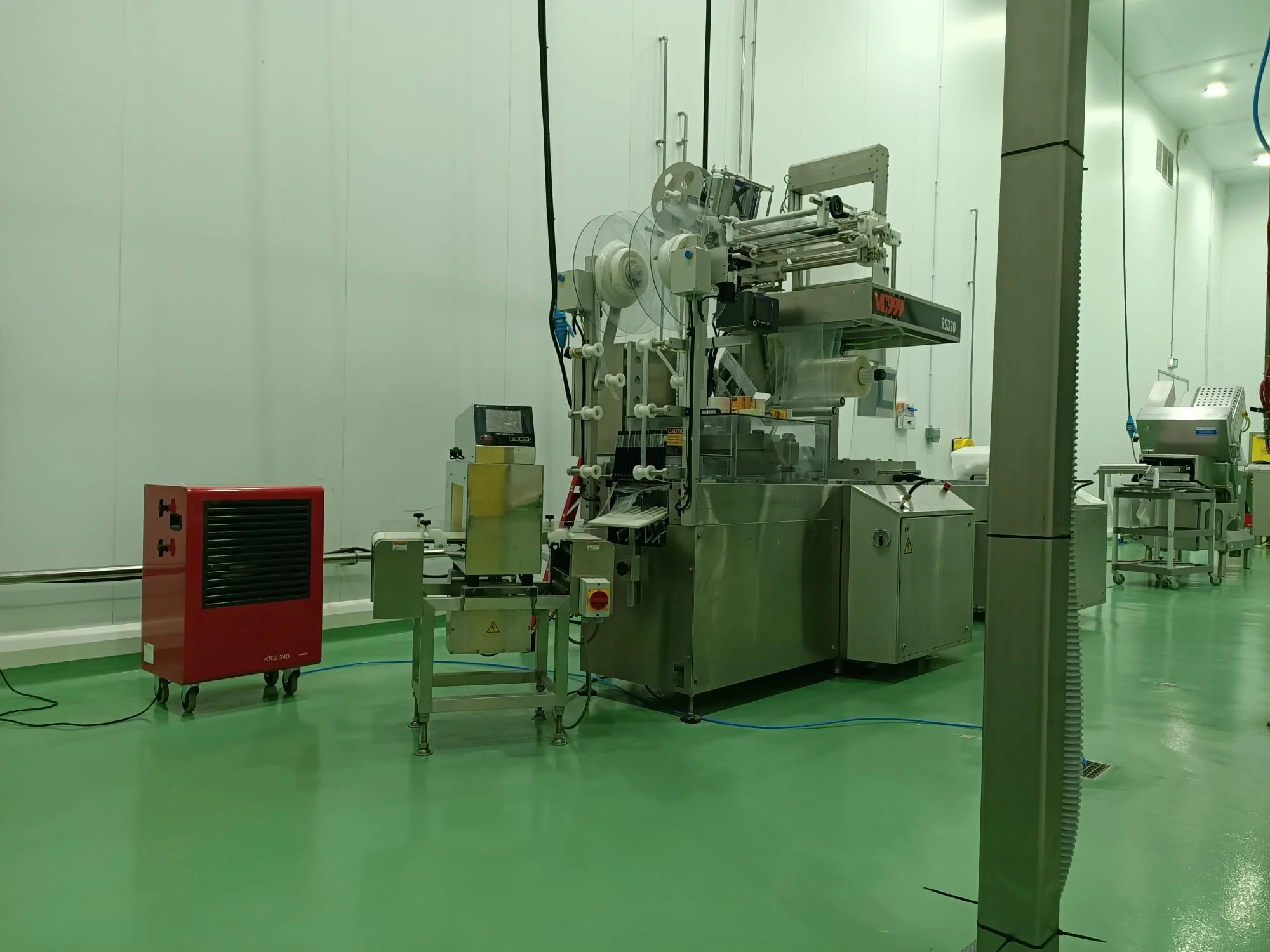 Industrial machine in a laboratory or manufacturing setting with green flooring and white walls.