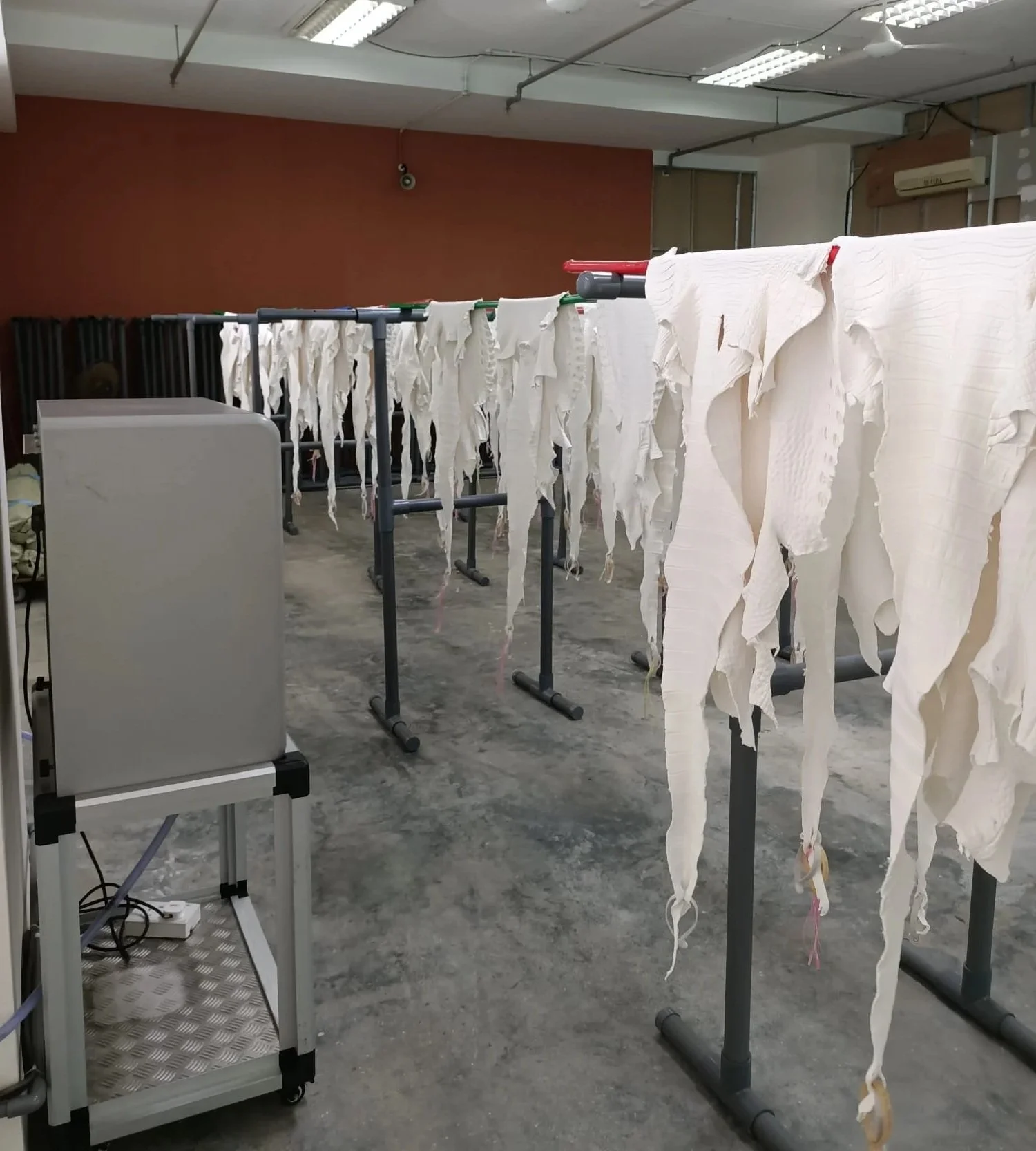 White leather fabric sheets hanging to dry on metal racks in an industrial laundry room.