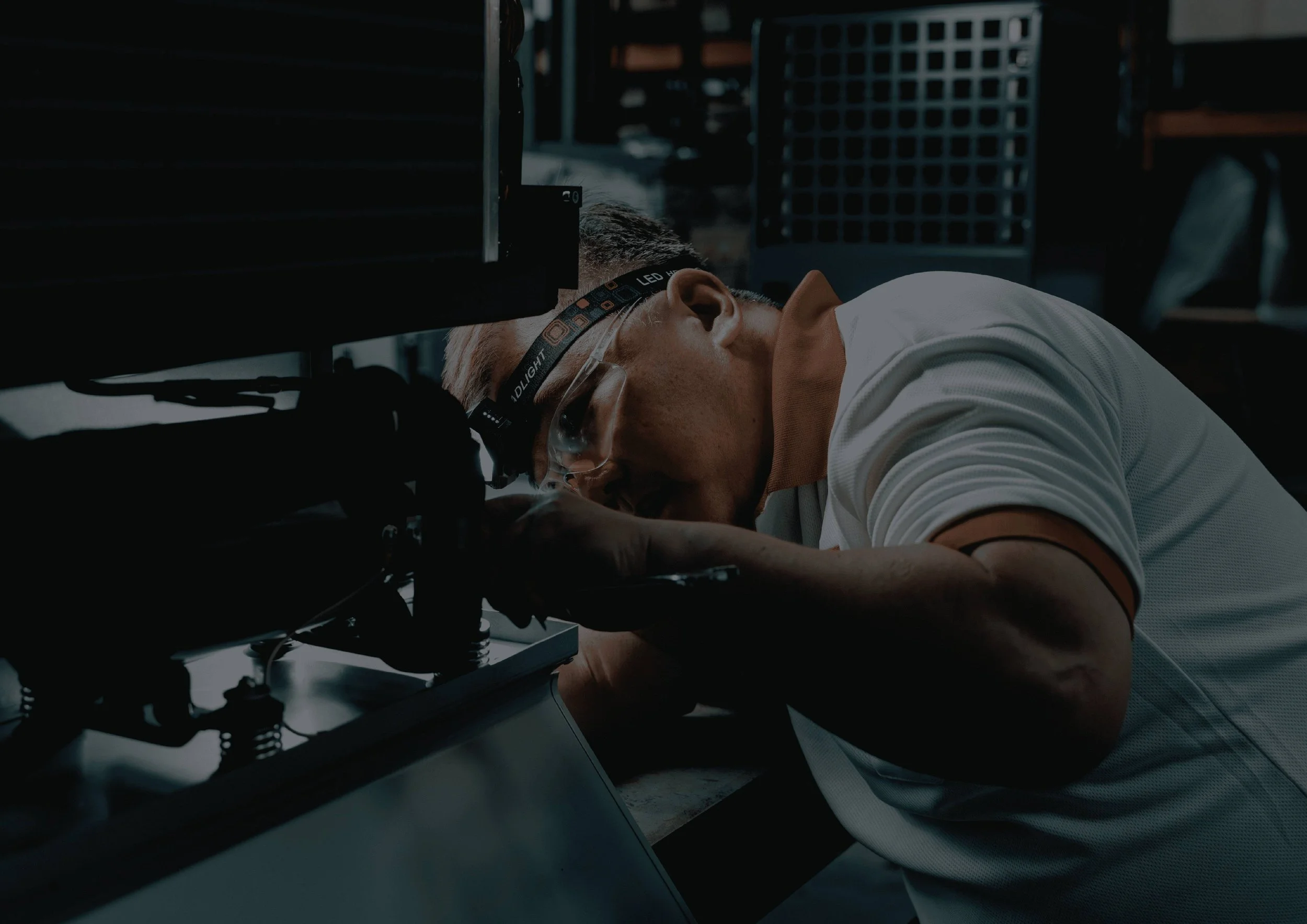 A man wearing a headlamp and glasses working on a dehumidifier unit in a industrial setting.