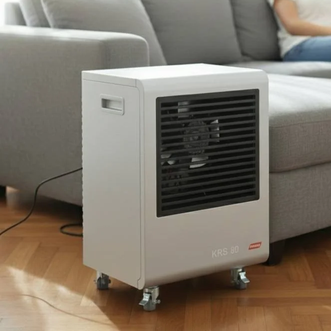 Portable dehumidifier placed on hardwood floor beside a gray sofa in a living room.