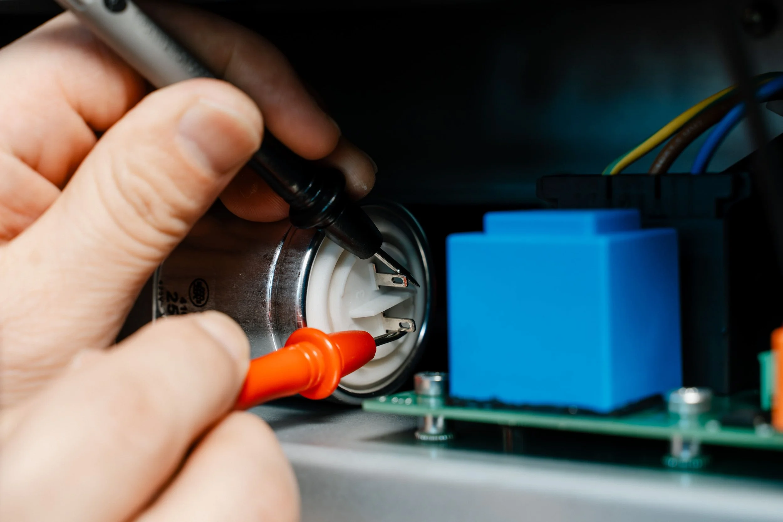 A person using tools to work on an electrical component inside a dehumidifier, with visible wiring and circuit board.