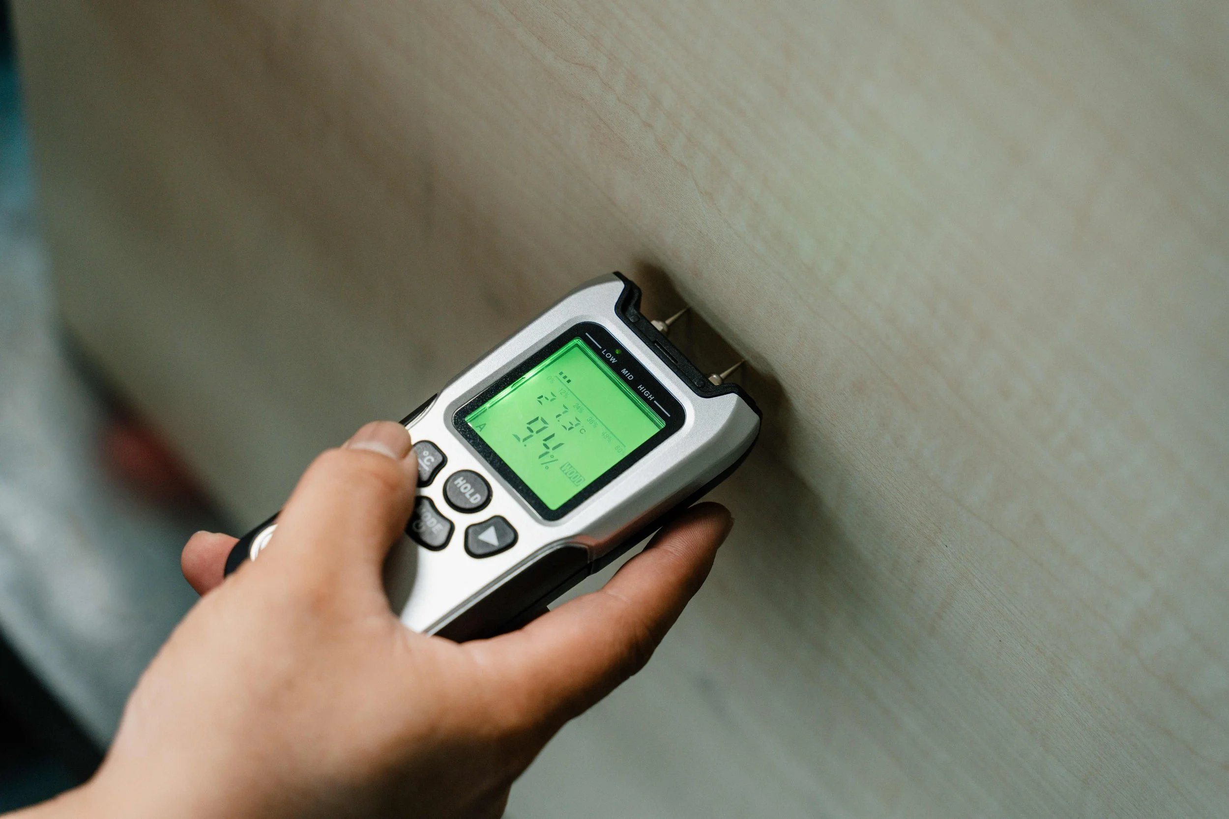 A person holding a digital infrared thermometer, aiming it at a wall to measure temperature.