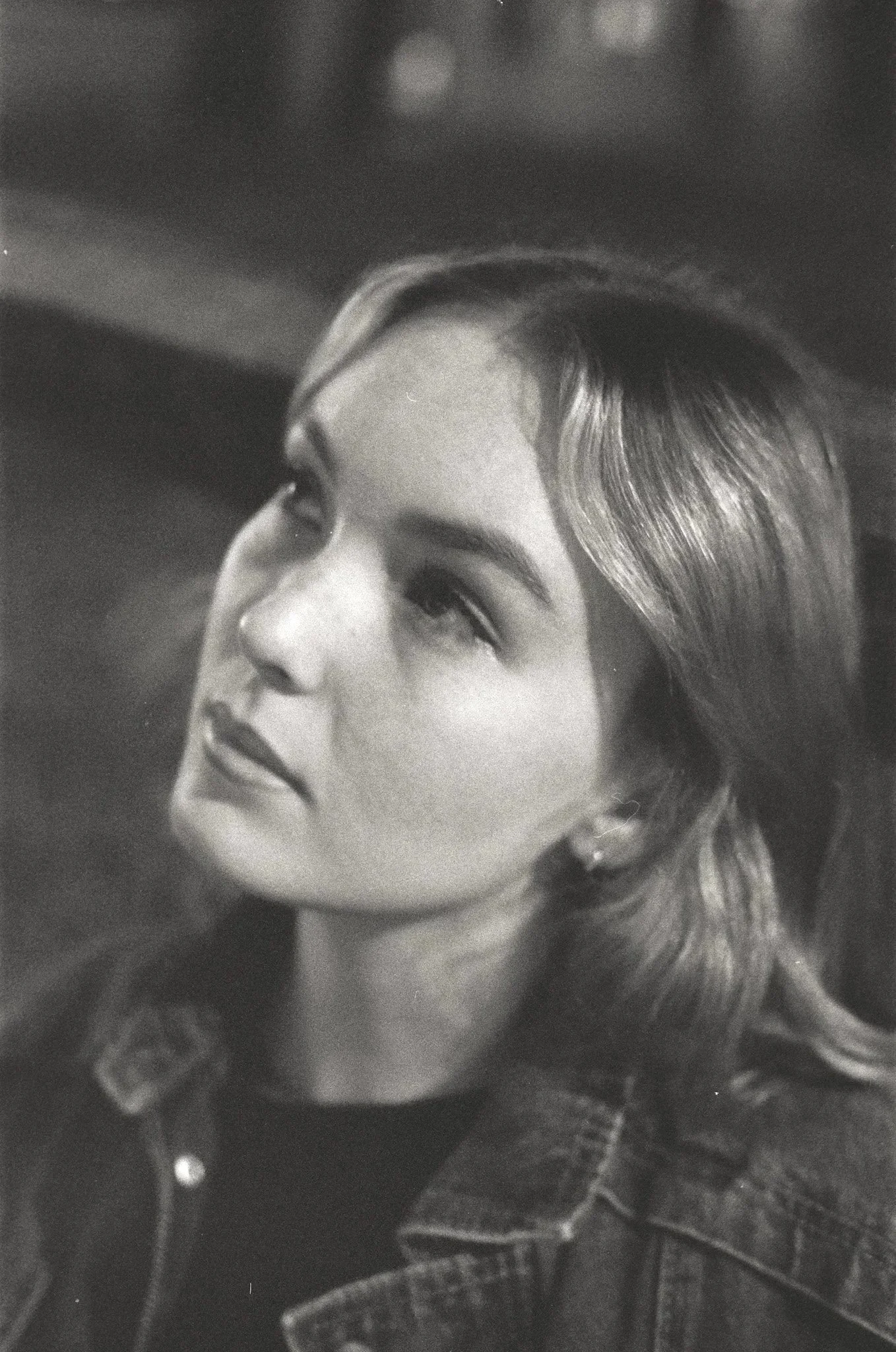 Black and white portrait of a young woman with wavy hair wearing a denim jacket, looking upward.