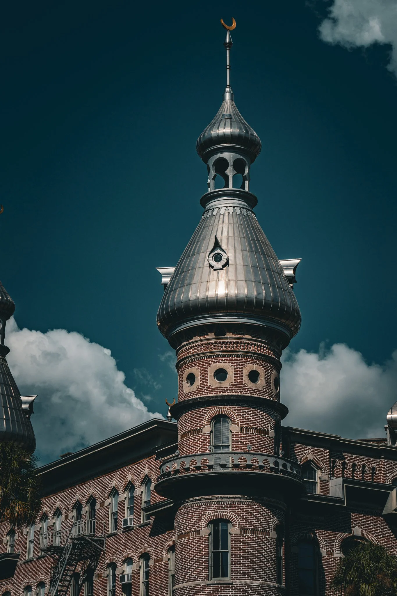 Photo of an ornate brick building with a tall, rounded, metal rooftop turret against a partly cloudy sky.