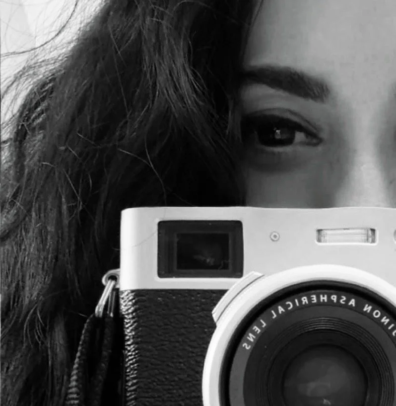 Close-up of a person with long dark hair holding a camera, with one eye partially visible.