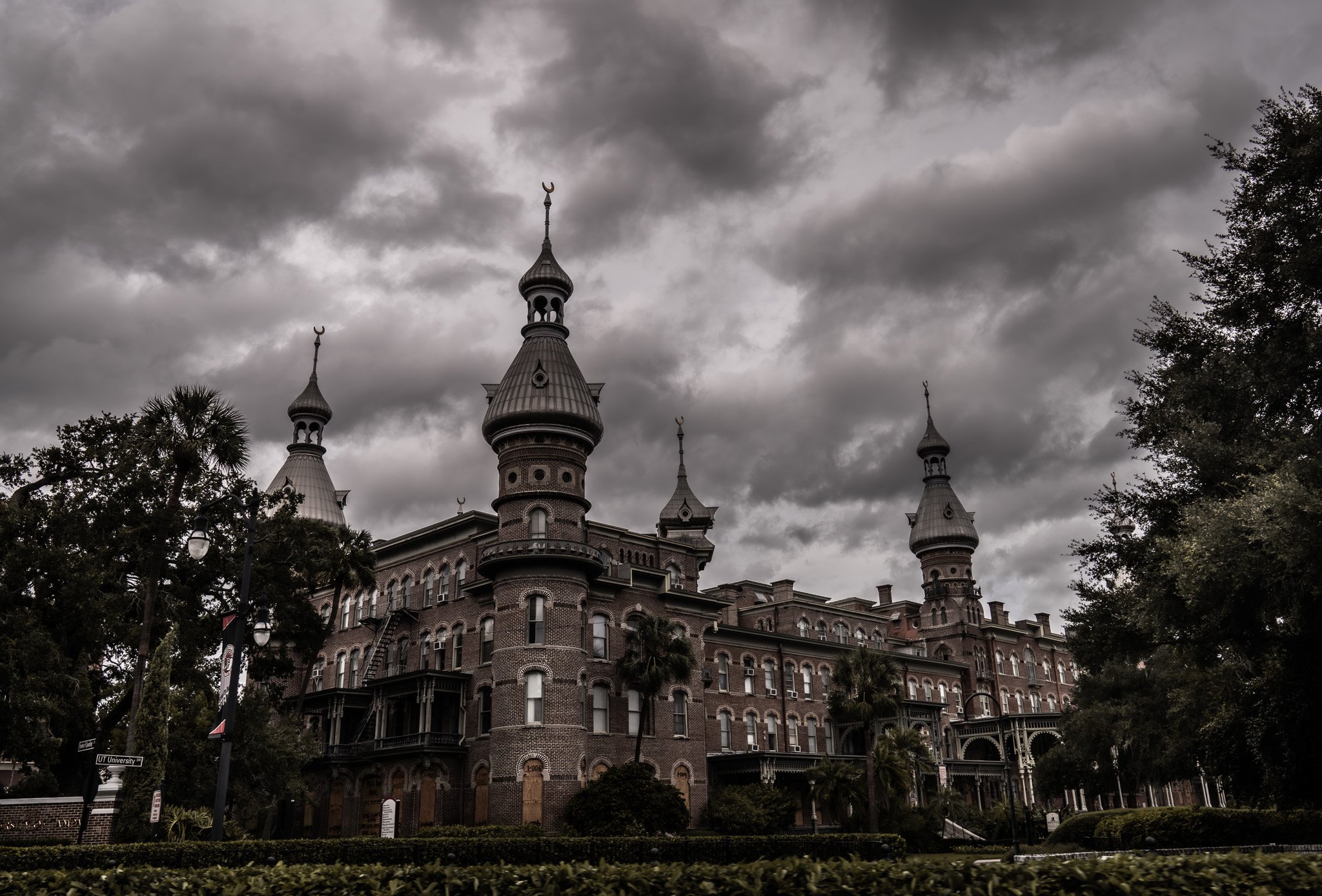 Henry B. Plant Museum, A historic castle-like mansion with turrets and towers under a dark, cloudy sky, surrounded by trees and bushes.