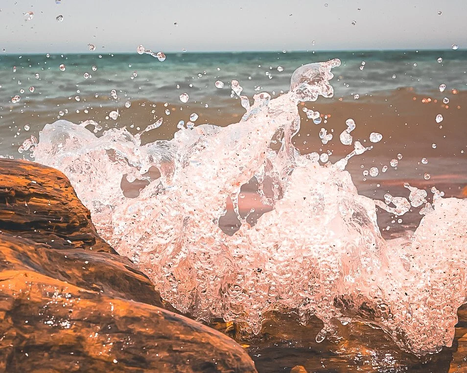 Waves crashing against rocks at the beach with a cloudy sky.