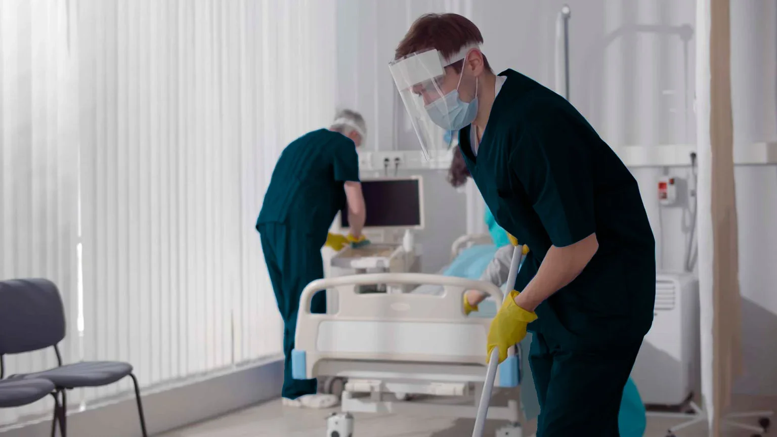 Healthcare workers in PPE cleaning a hospital room.